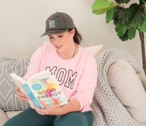 woman wearing a pink sweatshirt that says Mom on it while she's sitting on a couch reading a book