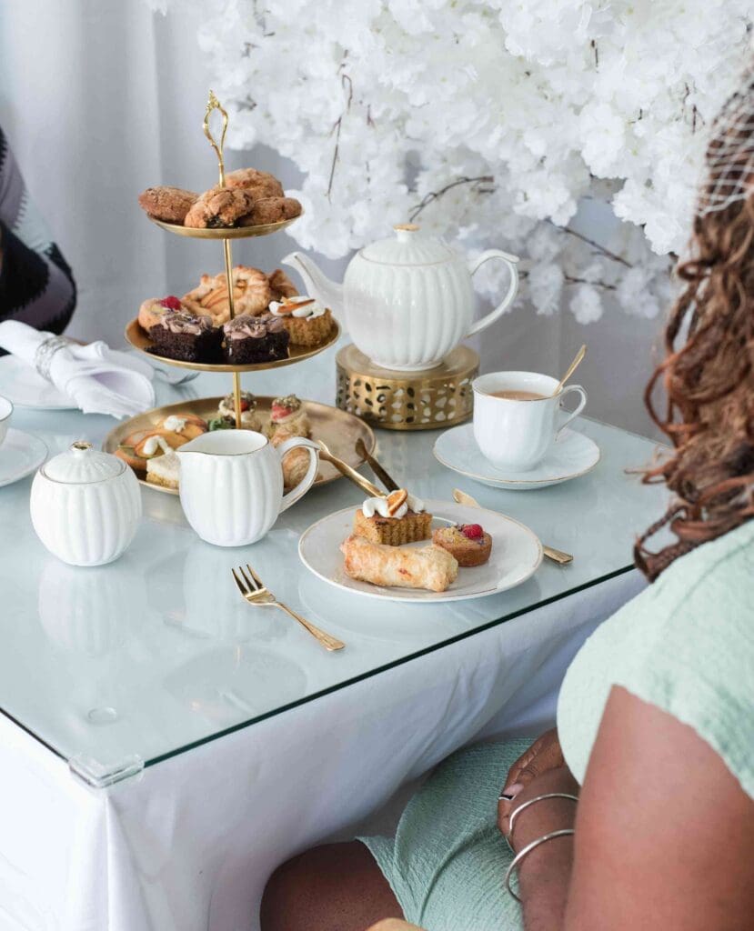 A person's back is to the camera while they look at a plate of pastries and a tiered stand with afternoon tea treats.