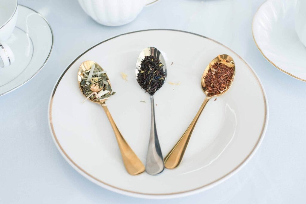 Tea room marketing photos for Kiona's Tea Room. A white plate holds three spoons with different kinds of loose-leaf tea: green, black, and rooibos.
